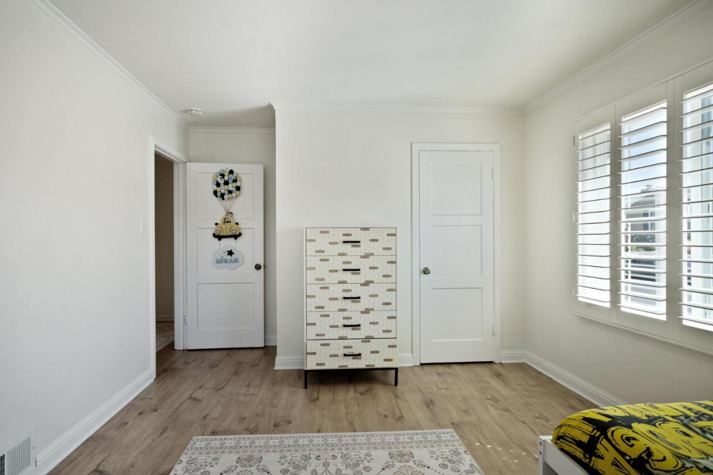 Bedroom with plantation shutters, a patterned chest of drawers, and yellow-and-black bedding.