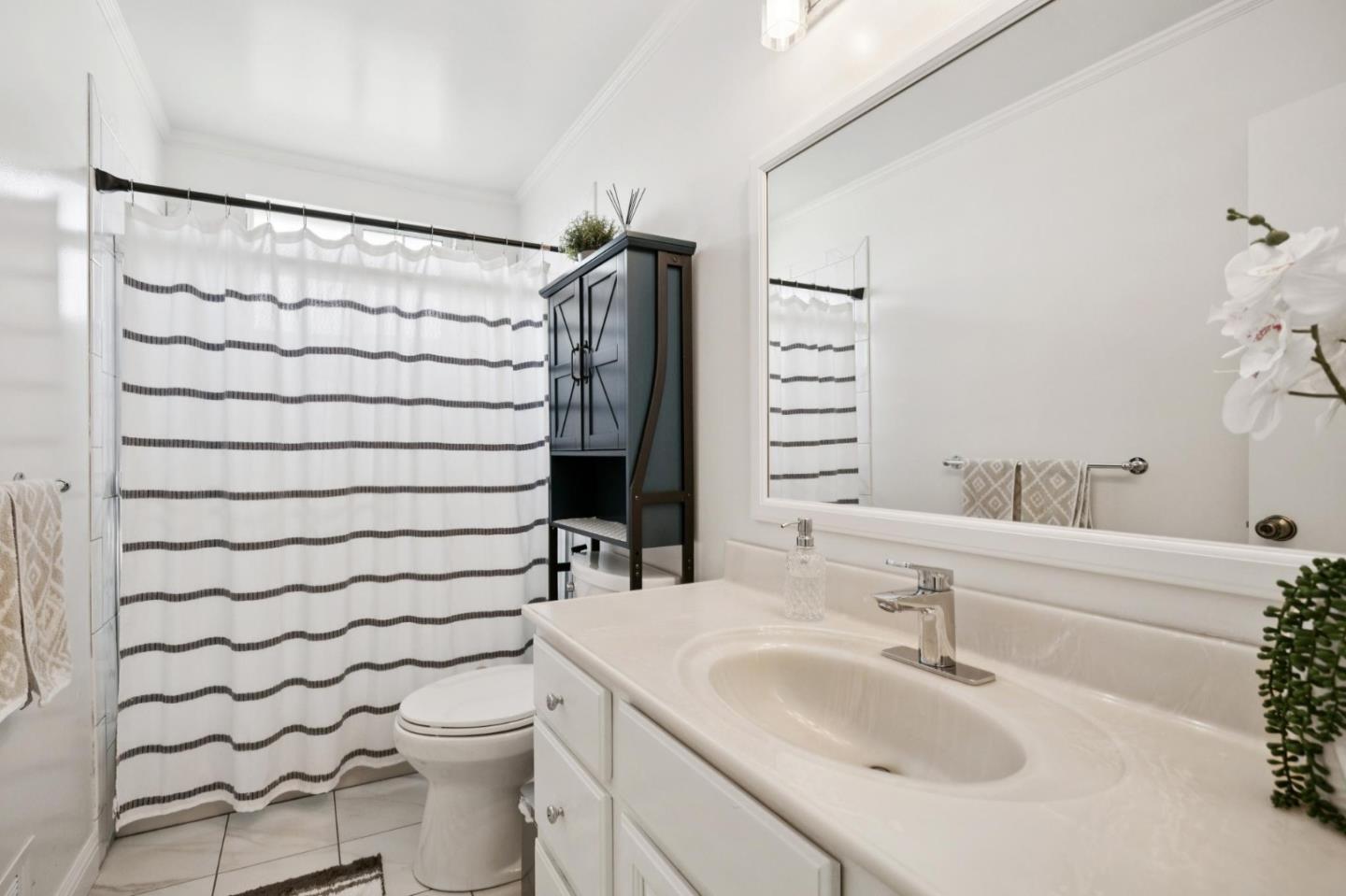 Bright bathroom with a white vanity, large mirror, toilet, and striped shower curtain.