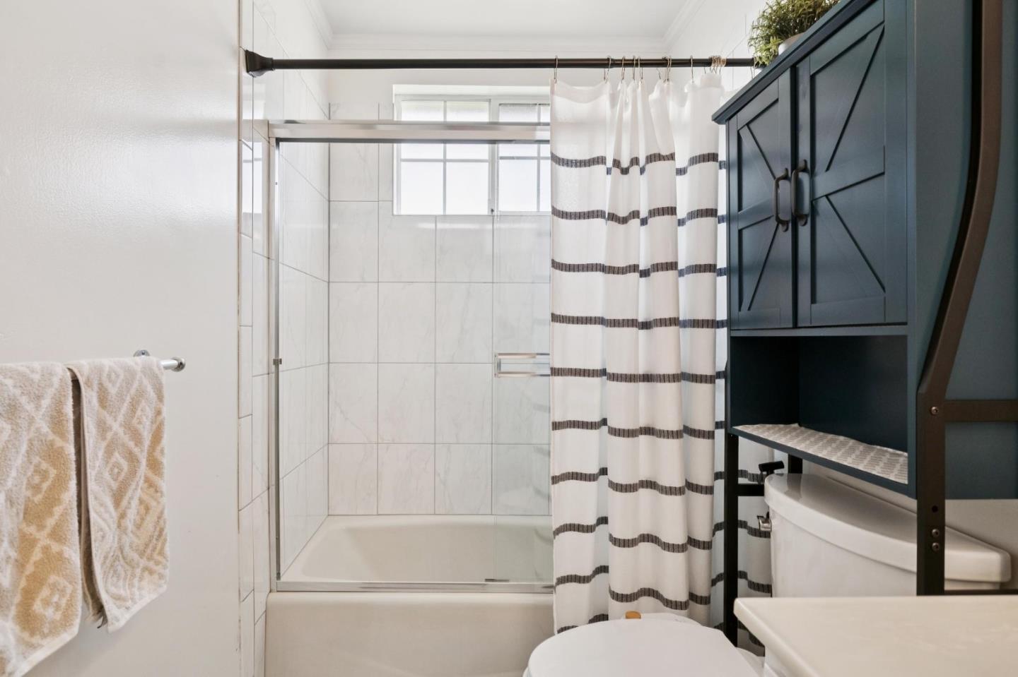 Bathroom with a tiled tub-shower, striped curtain, and dark blue storage cabinet.