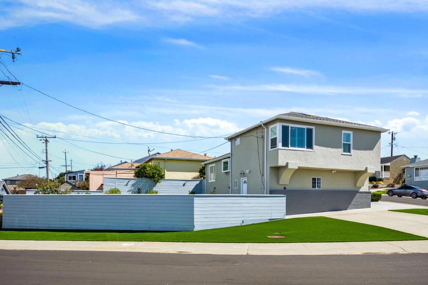 Two-story stucco home with blue shutters, a white fence, and a green front lawn.