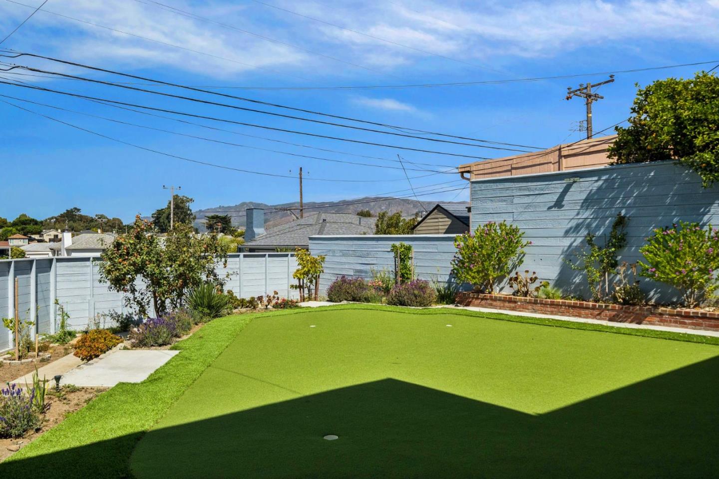 Backyard putting green bordered by blue fences and landscaped planting beds.