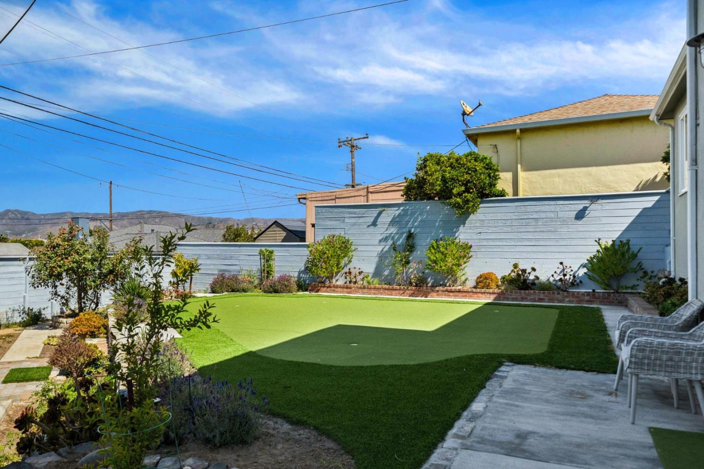 Backyard with artificial-turf lawn, landscaped garden beds, blue fence, and patio seating.