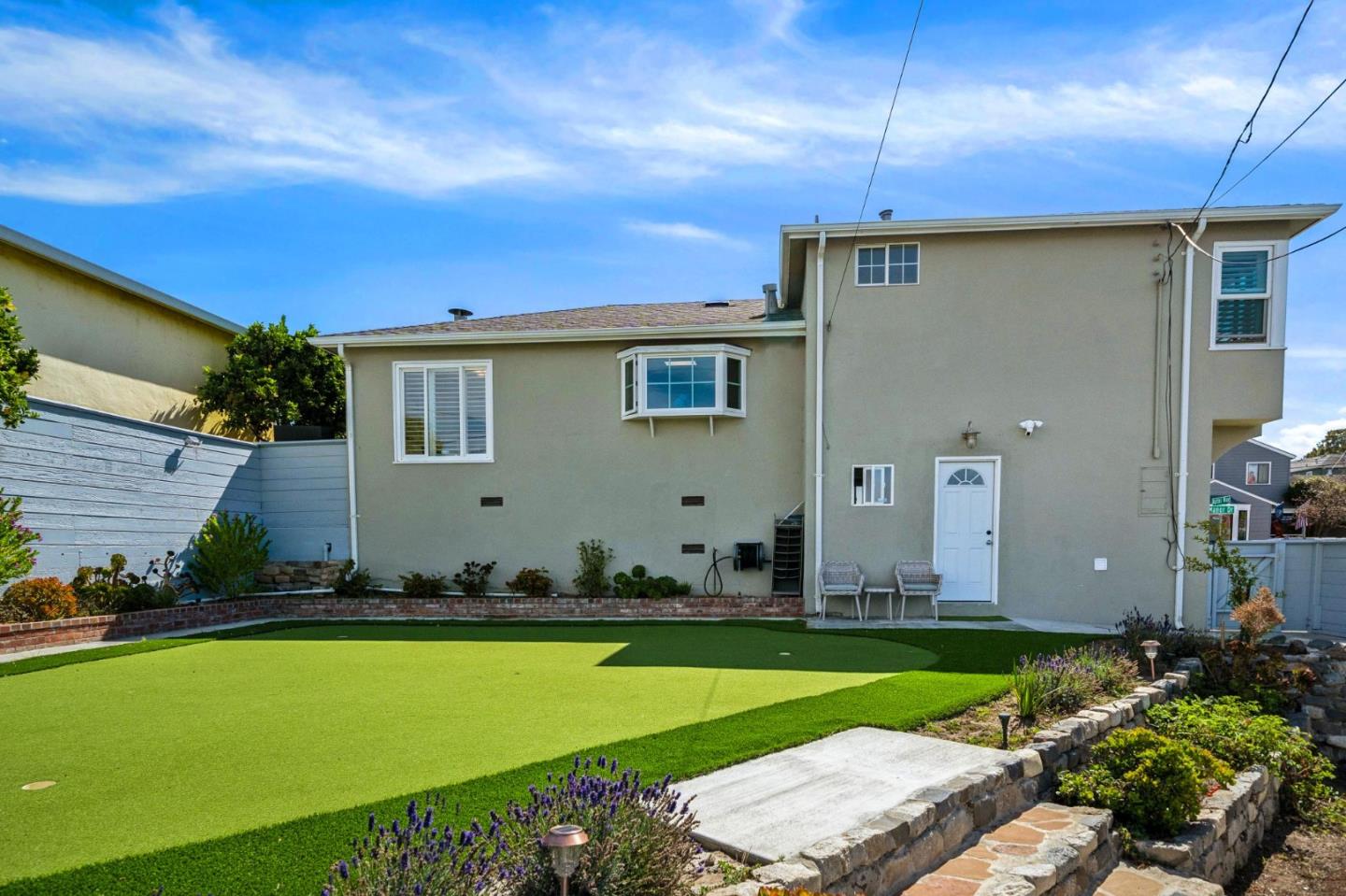 Two-story home with a landscaped artificial-turf lawn, stone garden beds, and a paved path.