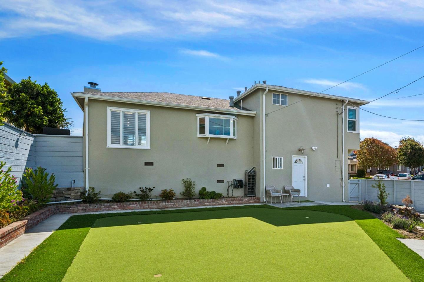 Rear exterior of a two-story home with a bay window and fenced artificial-turf yard.