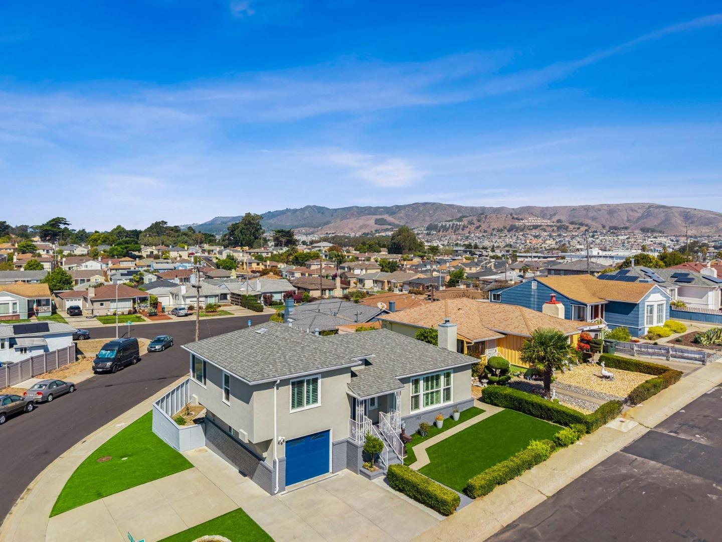 Corner house with a blue garage door and landscaped lawn, overlooking the neighborhood and distant hills.