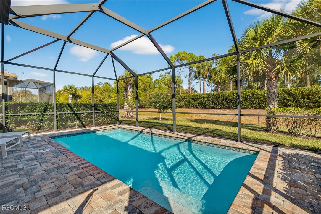 Swimming pool in a screened enclosure with a paver deck and palm trees beyond.