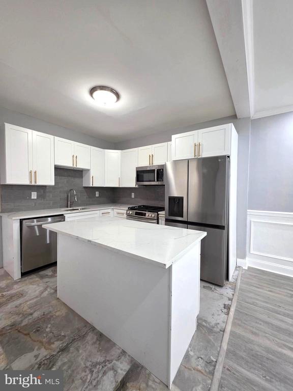 Kitchen with a large white island, stainless steel appliances, and gray tile backsplash.