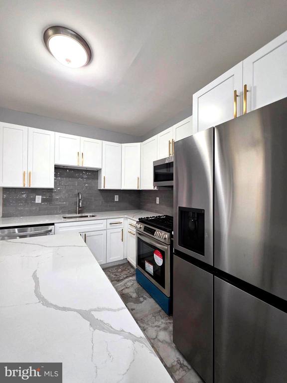 Modern kitchen with white cabinetry, gray tile backsplash, veined island, and stainless steel appliances.