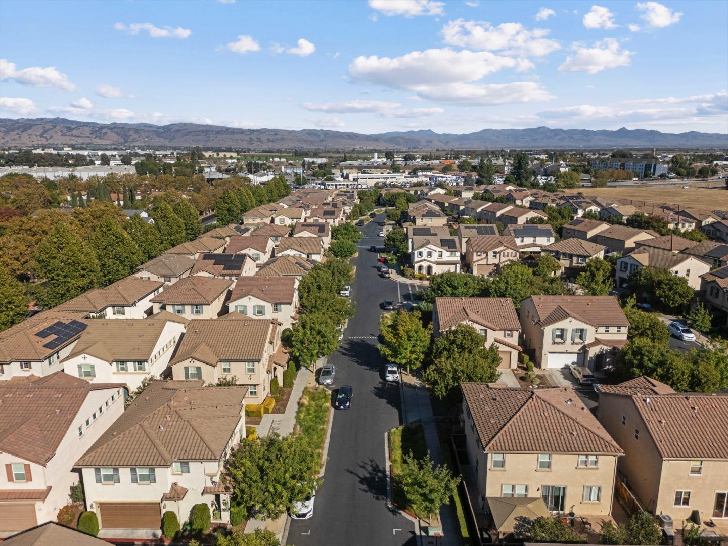 Aerial view of a residential neighborhood, with tiled-roof homes, a central street, and distant hills.