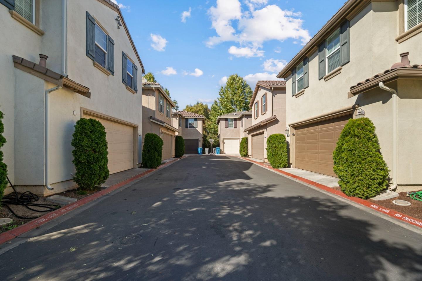 Attached homes line a paved lane, with garage doors, trimmed shrubs, and red fire-lane curbs.