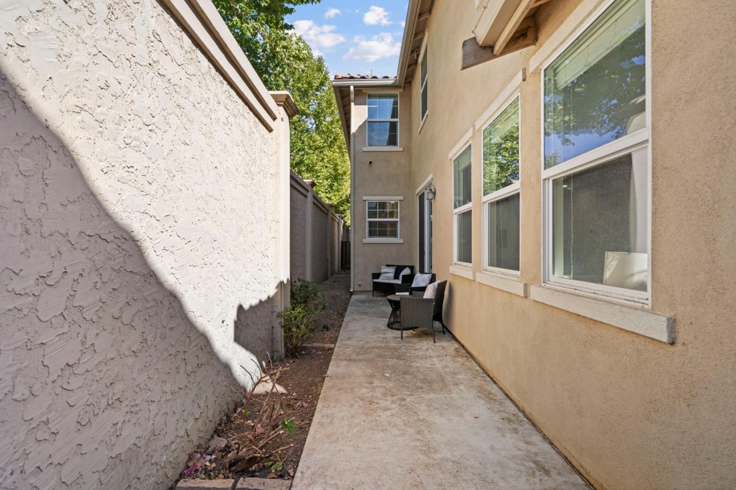 Side patio beside a two-story stucco home, with outdoor seating and a high boundary wall.