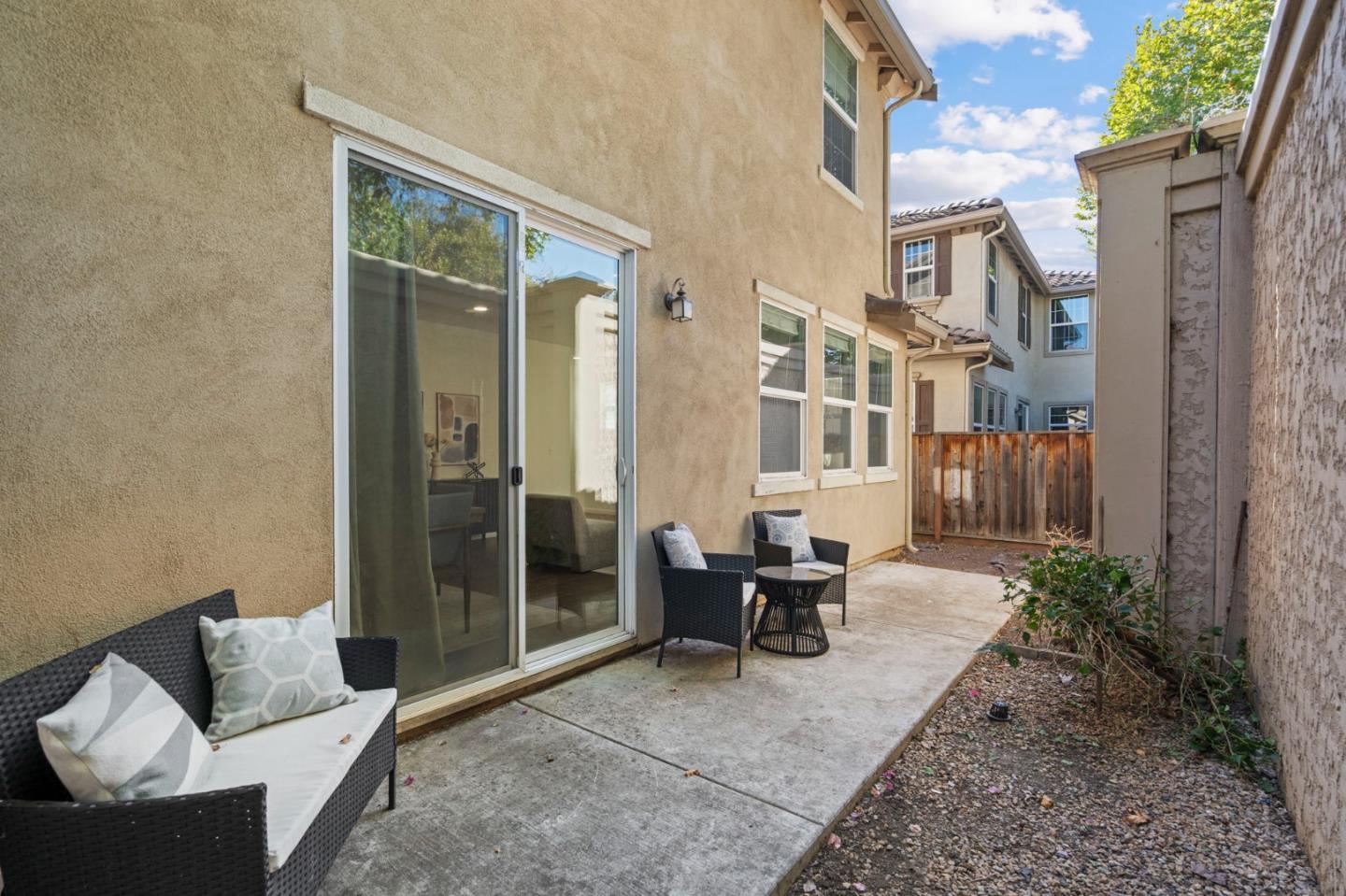 Side patio with wicker seating beside a beige home and sliding glass door.