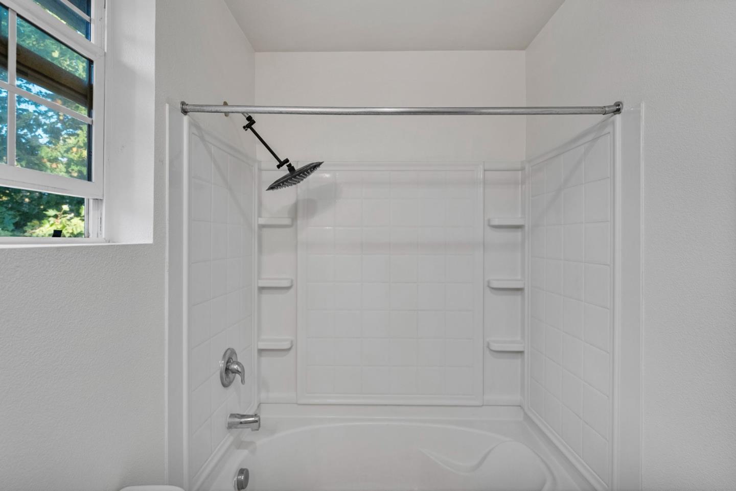 Bathroom shower and bathtub with a dark rainfall showerhead, built-in shelves, and a window.