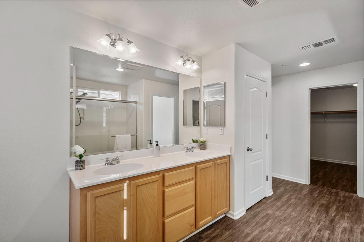 Bathroom with a double-sink vanity, light wood cabinets, and a glass-enclosed shower.