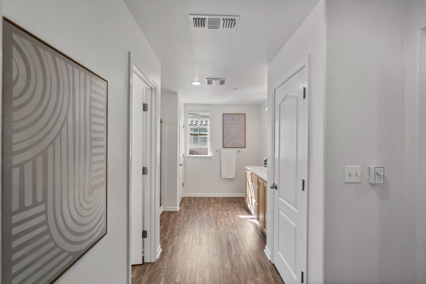Bright bathroom with a long wood-cabinet vanity, wood-look flooring, and a towel beneath the window.