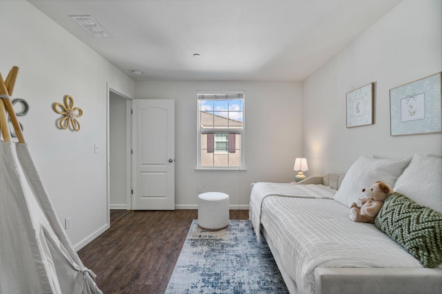 Bright bedroom with a white bed, blue patterned rug, and window overlooking a neighboring home.