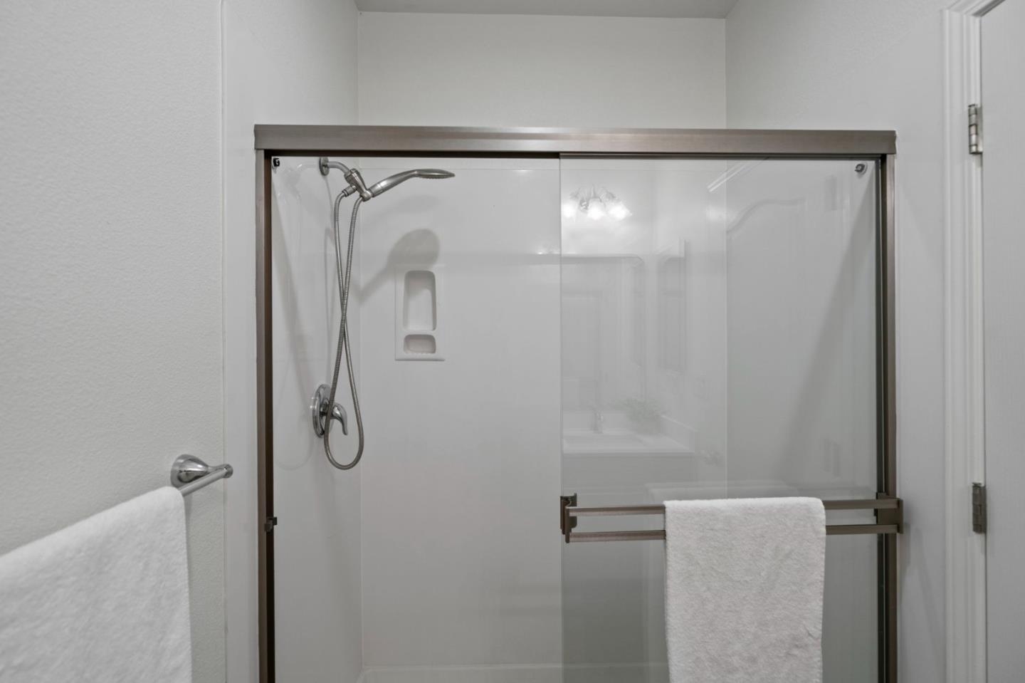 Bathroom shower with a glass enclosure, chrome handheld showerhead, recessed niche, and white towels.