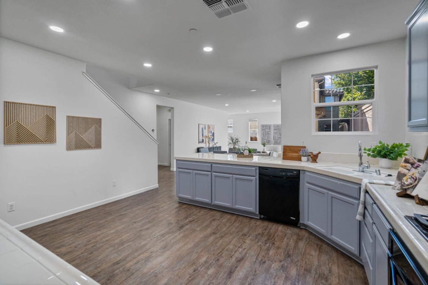 Open-plan kitchen with gray cabinets, white counters, and a large window overlooking greenery.