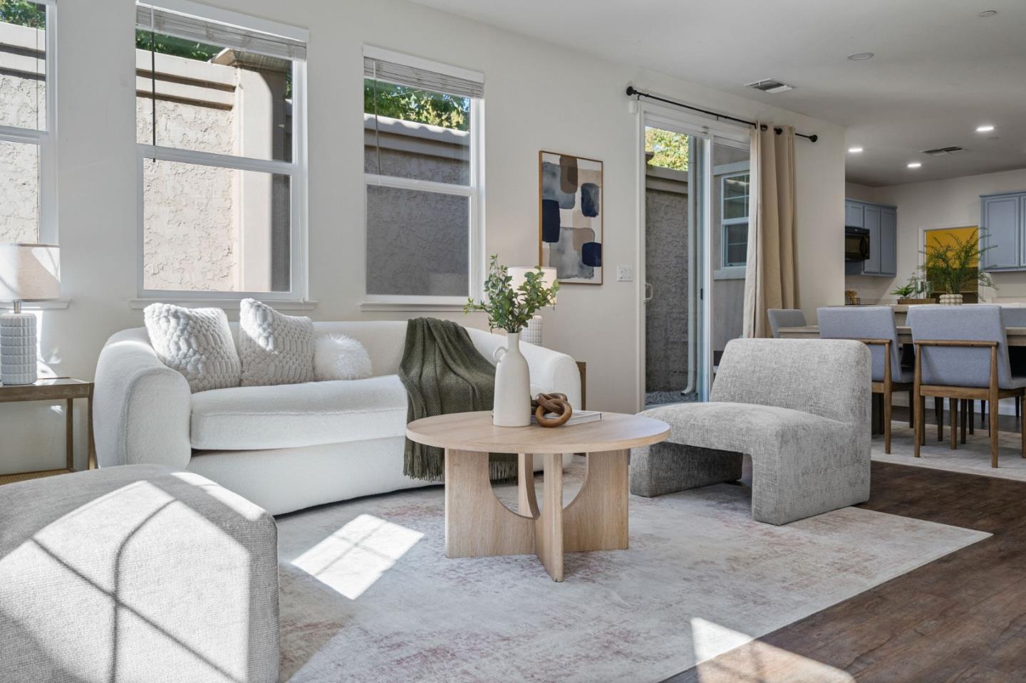 Staged living room with a white sofa, round wood coffee table, and dining area beside the kitchen.
