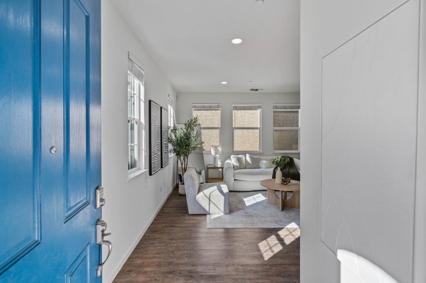 Living room viewed through a blue front door, with white sofas and dark wood floors.