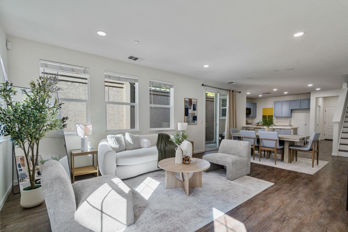 Staged open-plan living and dining area with pale blue kitchen cabinets and large windows.