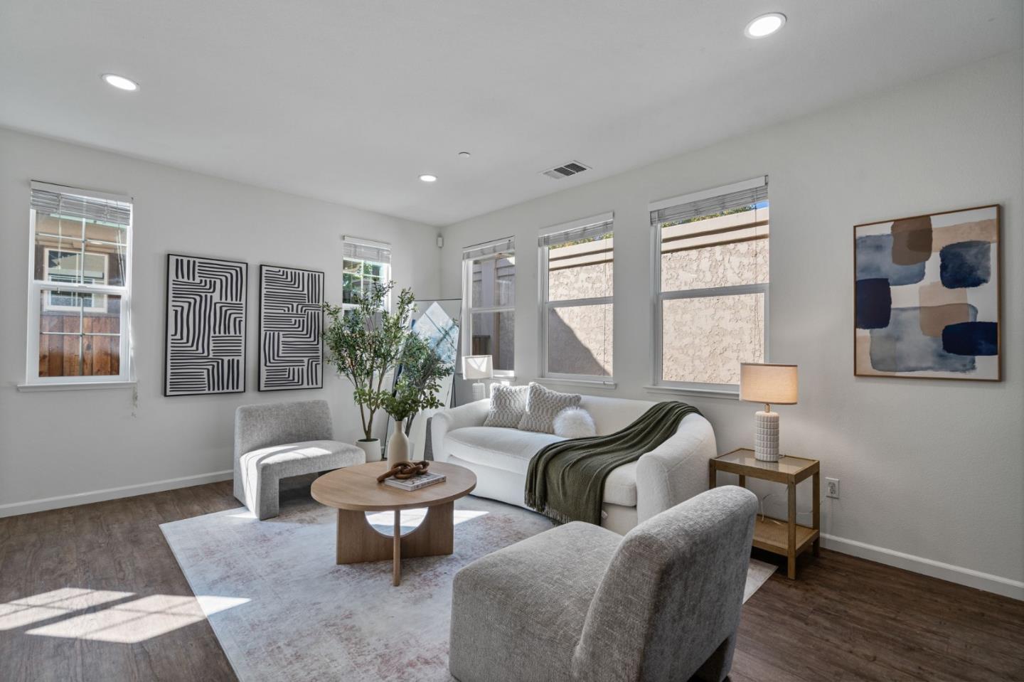 Bright staged living room with white sofas, gray chairs, and a round wood coffee table.