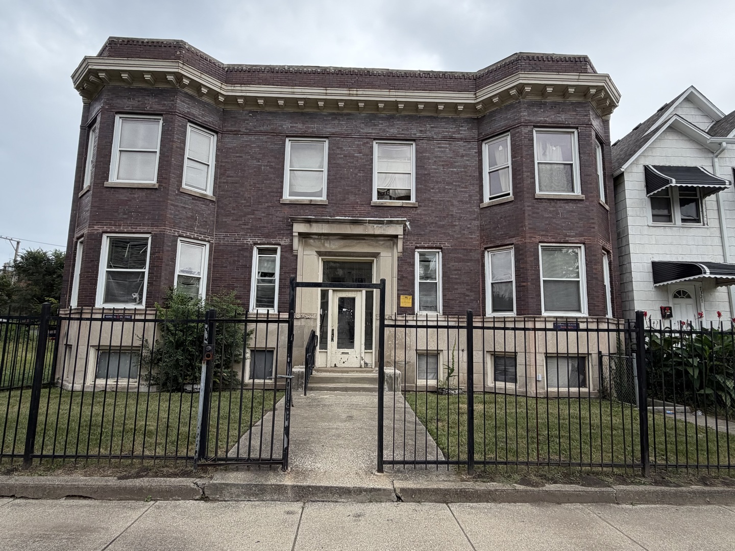 Dark red brick home with bay windows, a raised entrance, and a black metal fence.