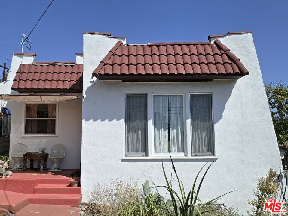 White stucco house with red tile roofs, red front steps, and a small porch with wicker chairs.