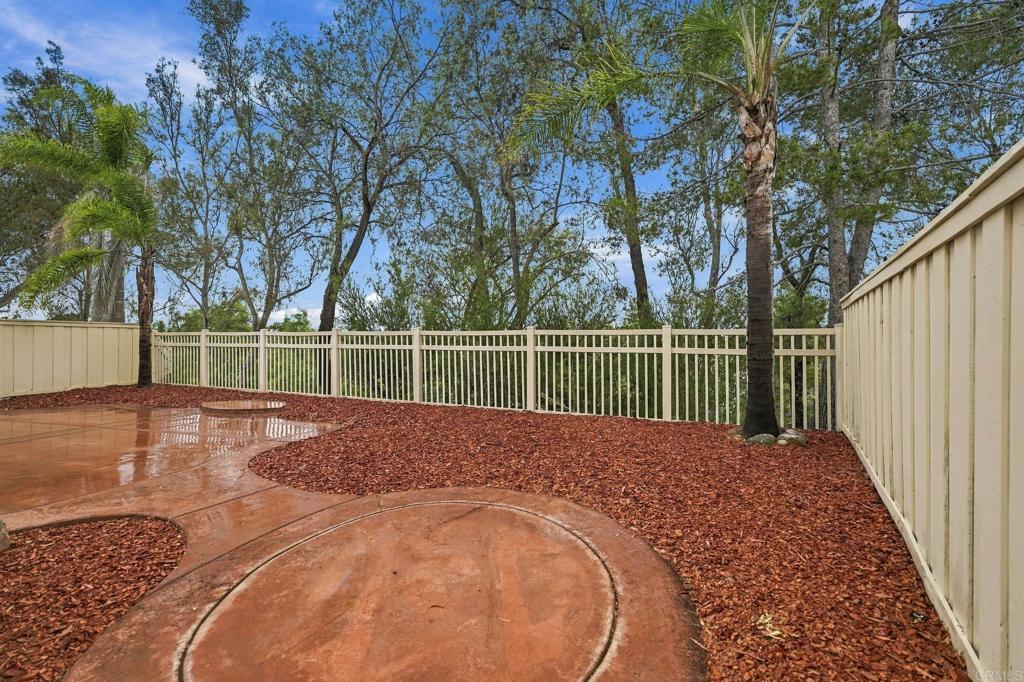 Fenced backyard patio with curved concrete paving, red mulch, and mature trees.
