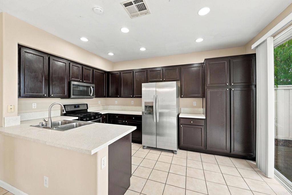 Kitchen with dark wood cabinets, stainless steel refrigerator, and a peninsula sink.