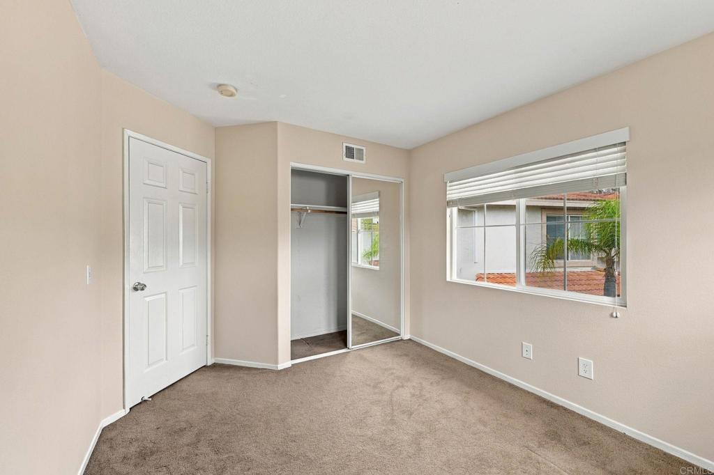 Empty bedroom with beige walls, brown carpet, an open closet, and a wide window with blinds.