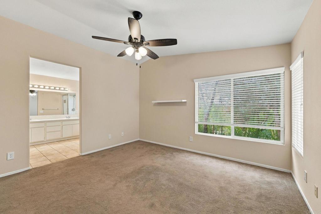 Unfurnished carpeted bedroom with a ceiling fan, wide window, and doorway to a bathroom.