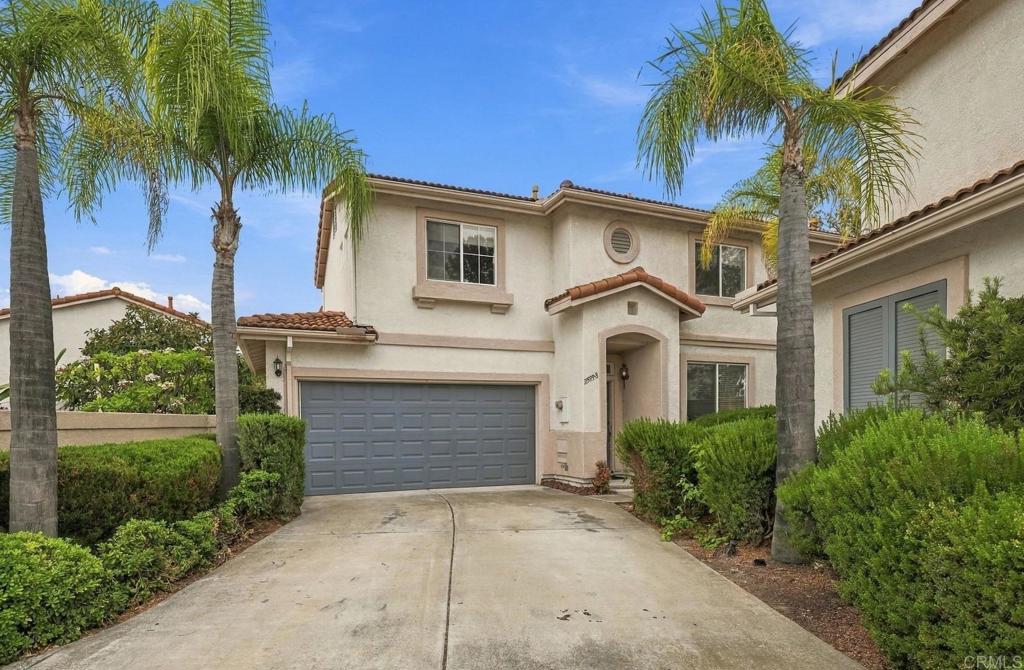 Two-story stucco home with a gray double garage, arched entry, and palm trees.