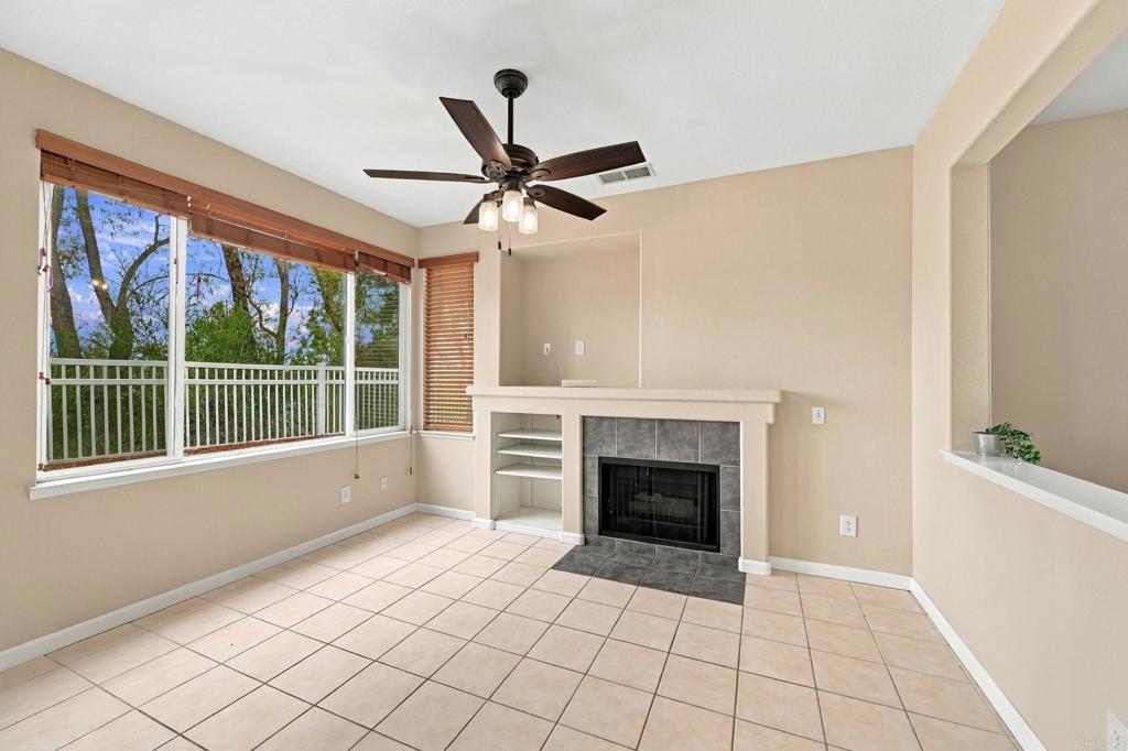 Living room with a tiled fireplace, built-in shelves, and large windows overlooking trees.