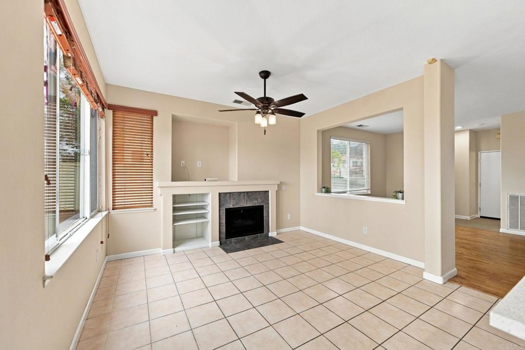 Empty living room with tiled floor, fireplace, ceiling fan, and large windows.