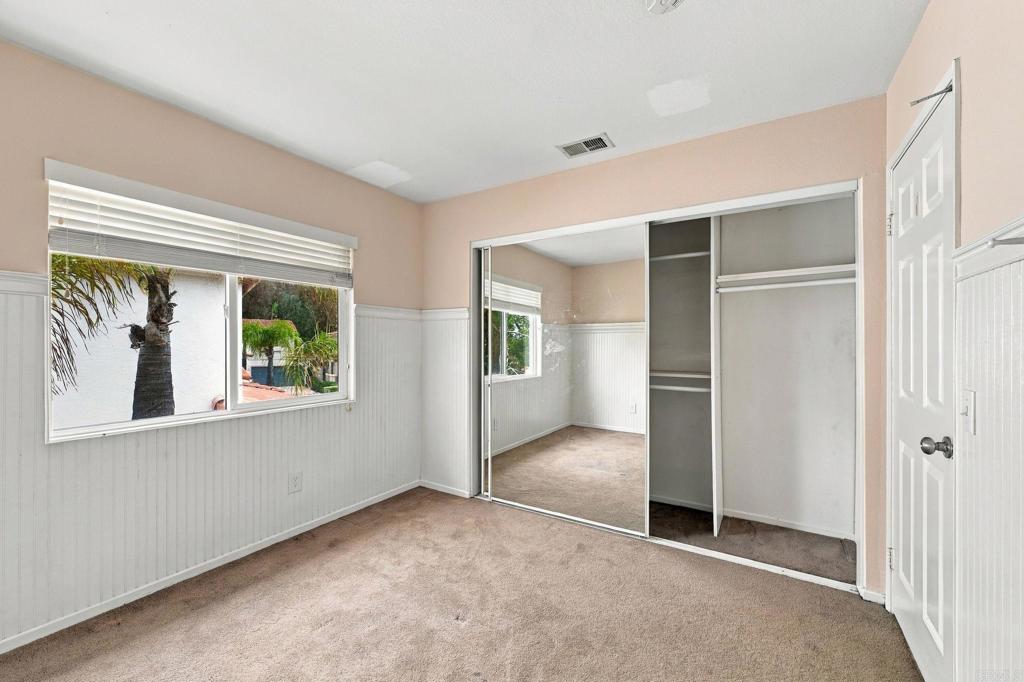 Empty bedroom with beige carpet, a window with blinds, and a sliding-door closet.
