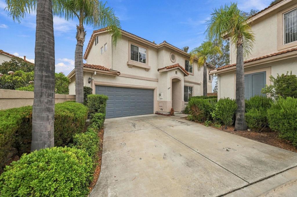 Two-story stucco home with a gray garage door, wide driveway, and palm trees.