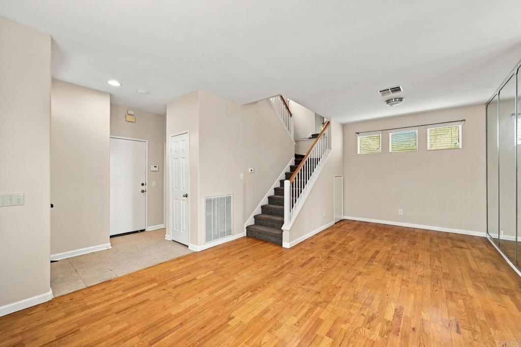Vacant living area with hardwood floors, carpeted staircase, and mirrored closet doors.