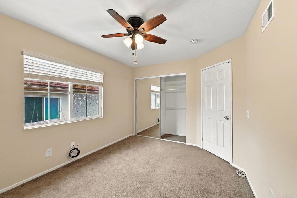 Unfurnished bedroom with mirrored closet doors, beige carpet, and a ceiling fan.
