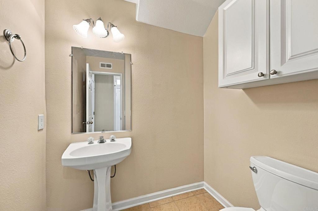 Bathroom with a pedestal sink, rectangular mirror, white wall cabinets, and tan tile floor.