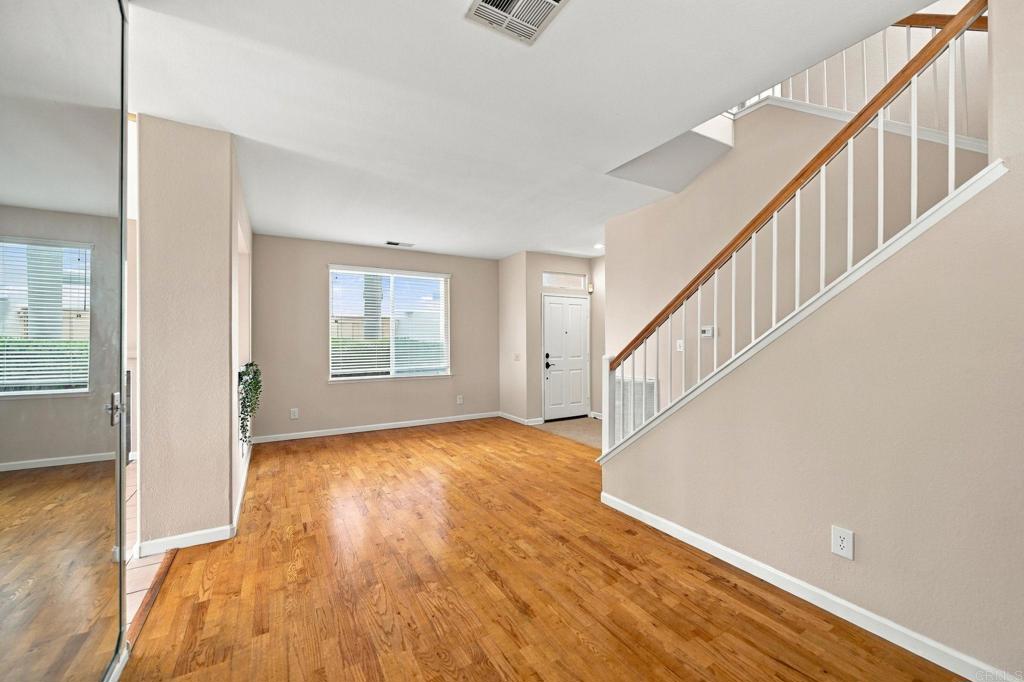 Unfurnished living area with hardwood floors, a large window, and a staircase with a wood handrail.