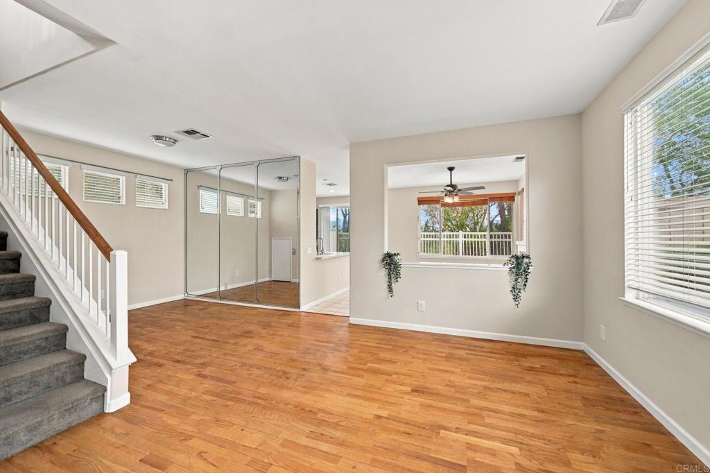 Empty living area with wood floors, carpeted staircase, mirrored doors, and windows overlooking trees.