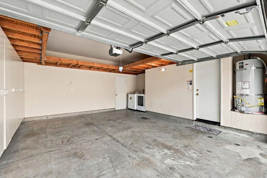 Empty garage with an open overhead door, exposed wood beams, washer and dryer, and water heater.