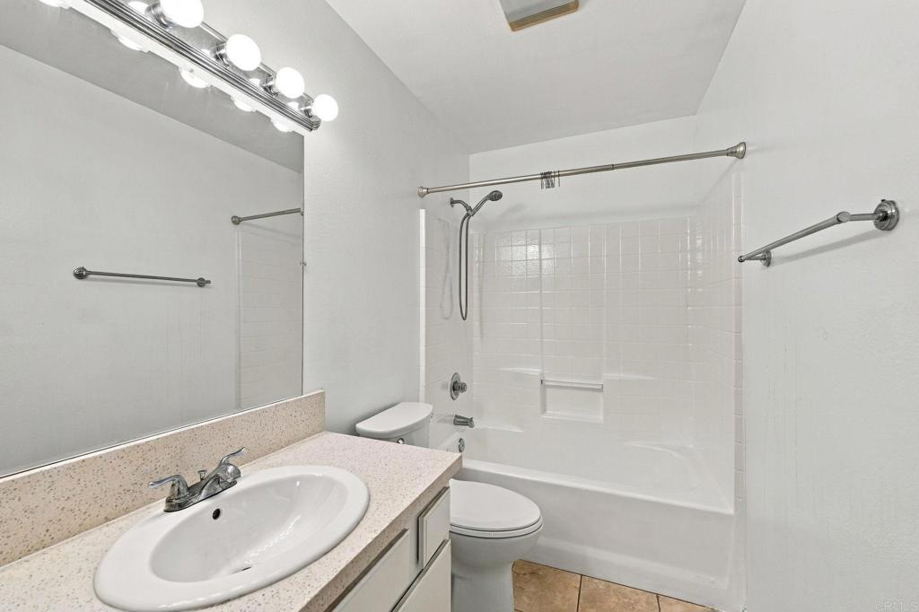 Bathroom with speckled vanity, oval sink, and white tiled tub and shower.