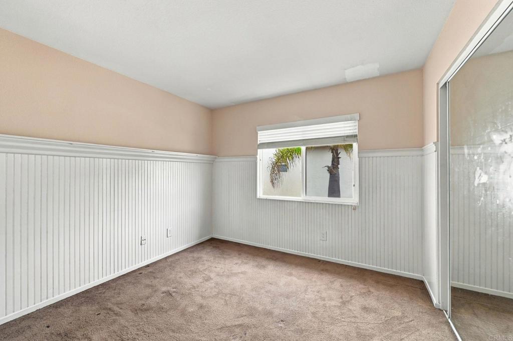 Empty carpeted room with white beadboard wainscoting, a window, and mirrored closet doors.