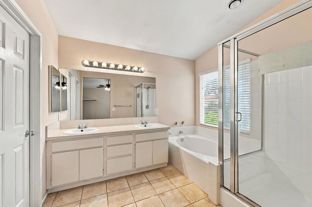 Bathroom with a double-sink vanity, bathtub, and glass-enclosed shower beside a window.