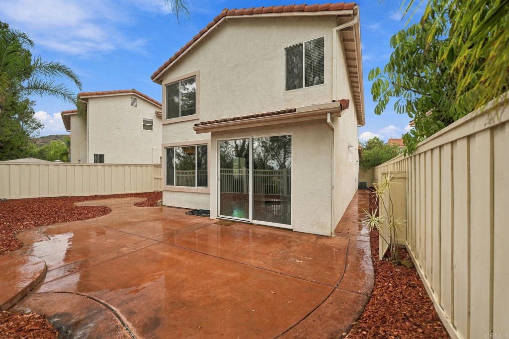 Two-story stucco home viewed from a wet concrete patio in a fenced backyard.