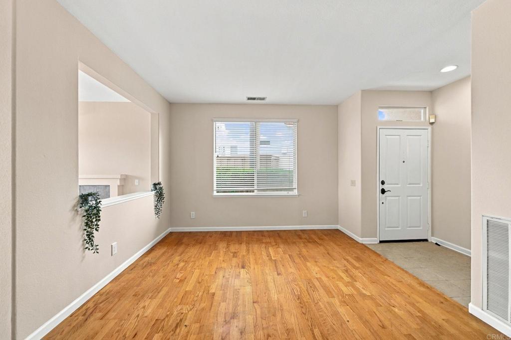 Empty room with hardwood floors, a large window, and a white entry door.