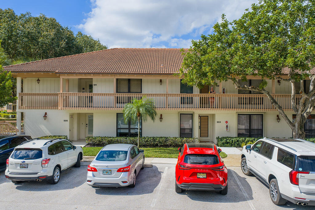 Two-story residential building with a long balcony, tiled roof, and cars parked in front.