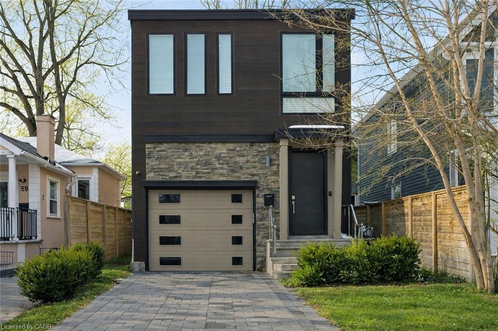 Modern two-story home with dark siding, stone facade, beige garage door, and paved driveway.